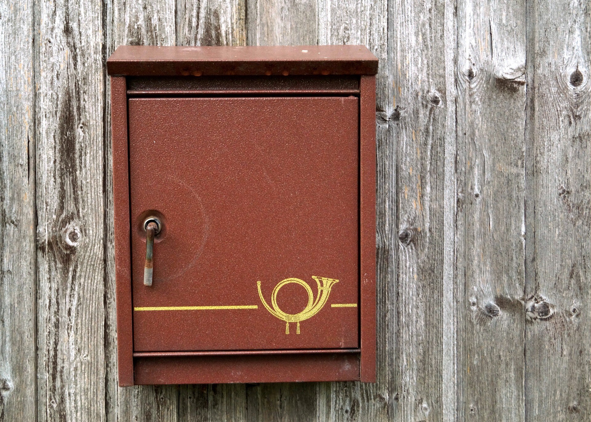 dark red letter box with gold detail hanging on a wooden fence